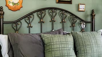 Een bed met een metalen hoofdbord, meerdere kussens en een bloemen decoratie aan de muur.