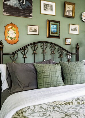 A bed with a metal headboard, multiple pillows, and a floral wall decoration.