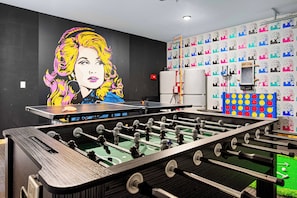 A room with a foosball table, a ping pong table, and a wall with a large pop art mural. - Heated Pool, Arcades, Hot Tub, Sauna, Dolly Vibes (Sevierville)