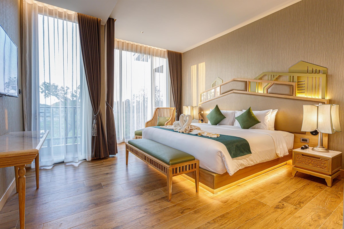 Habitación de hotel con una cama grande, lámparas de noche, un banco de madera, un escritorio y vistas al exterior a través de las ventanas.