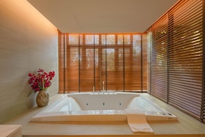 Un baño moderno con una bañera independiente, persianas de madera y un florero con flores.
