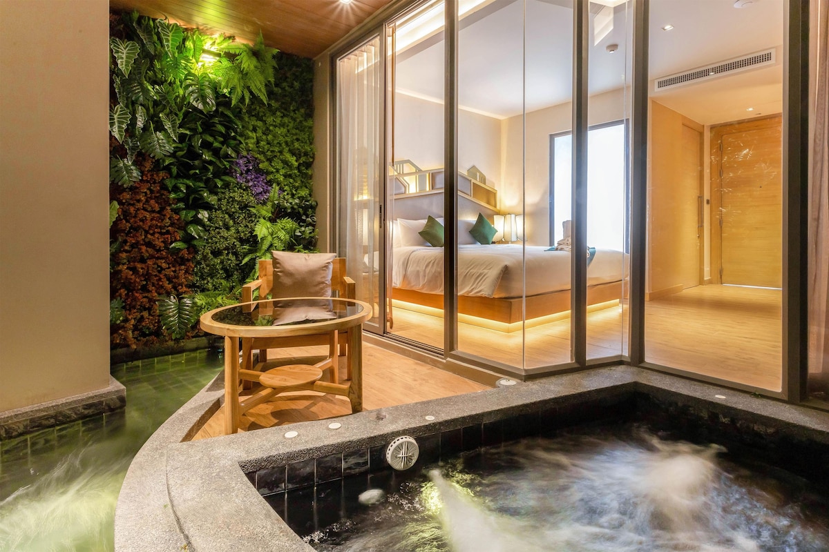 Un área de spa con un jacuzzi, una silla de madera y una habitación con paredes de vidrio que incluye una cama y un baño.
