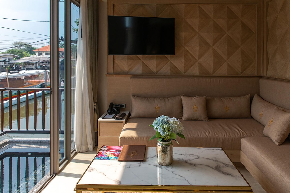 Habitación de hotel con un ventanal grande, un sofá, una mesita de centro y un televisor montado en la pared.