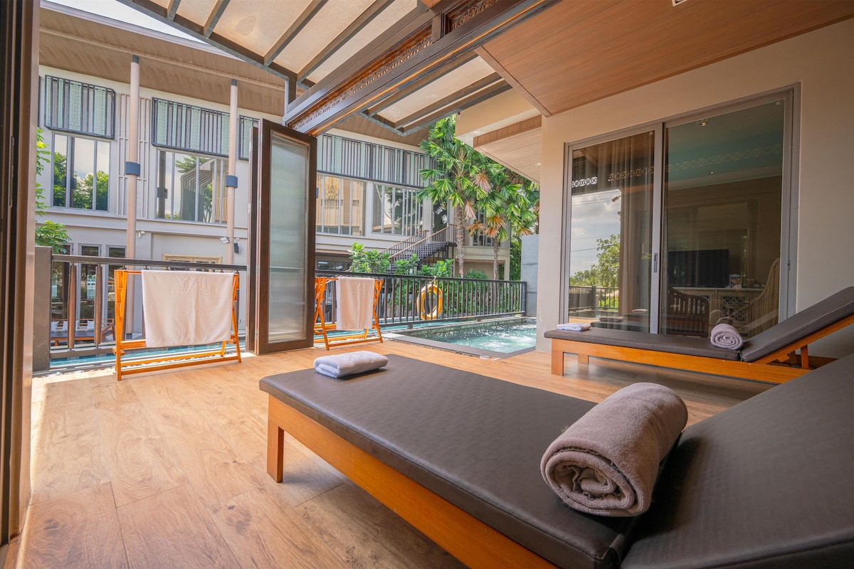 Habitación de hotel moderna con balcón, piscina y zona de estar con tumbonas.
