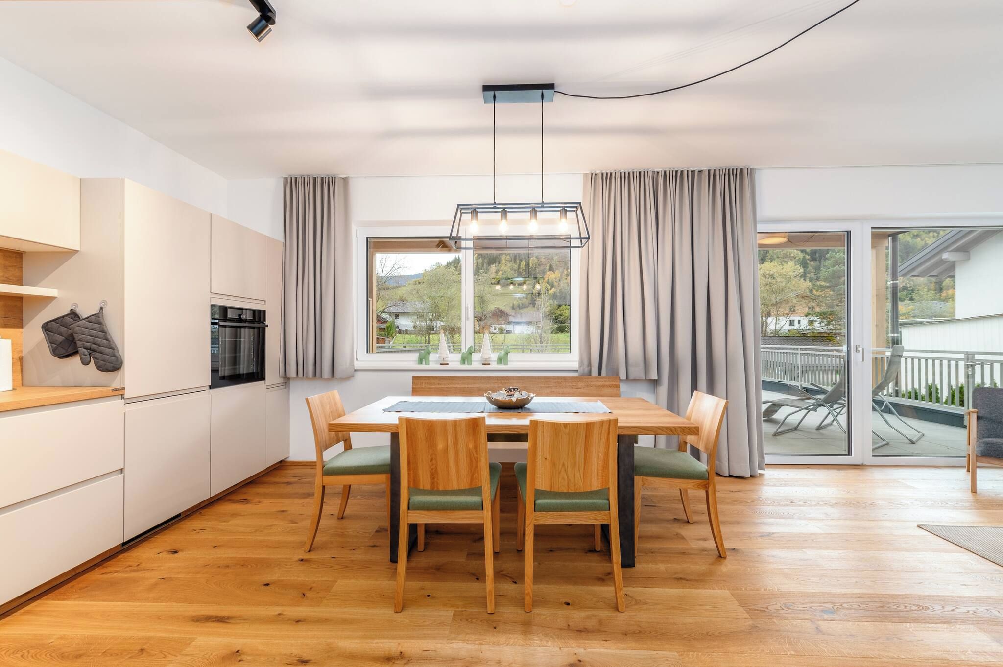 A modern kitchen with a dining area, wooden flooring, and a view of a balcony.
