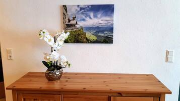 Eine Holzkommode mit einer Vasen voller weißer Orchideen und einem Landschaftsbild an der Wand.