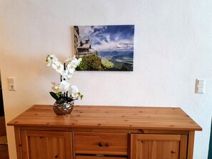 Eine Holzkommode mit einer Vasen voller weißer Orchideen und einem Landschaftsbild an der Wand.