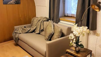 Ein gemütliches Wohnzimmer mit einer Couch, einem kleinen Holztisch, einer Lampe und einem Fenster mit Vorhängen.