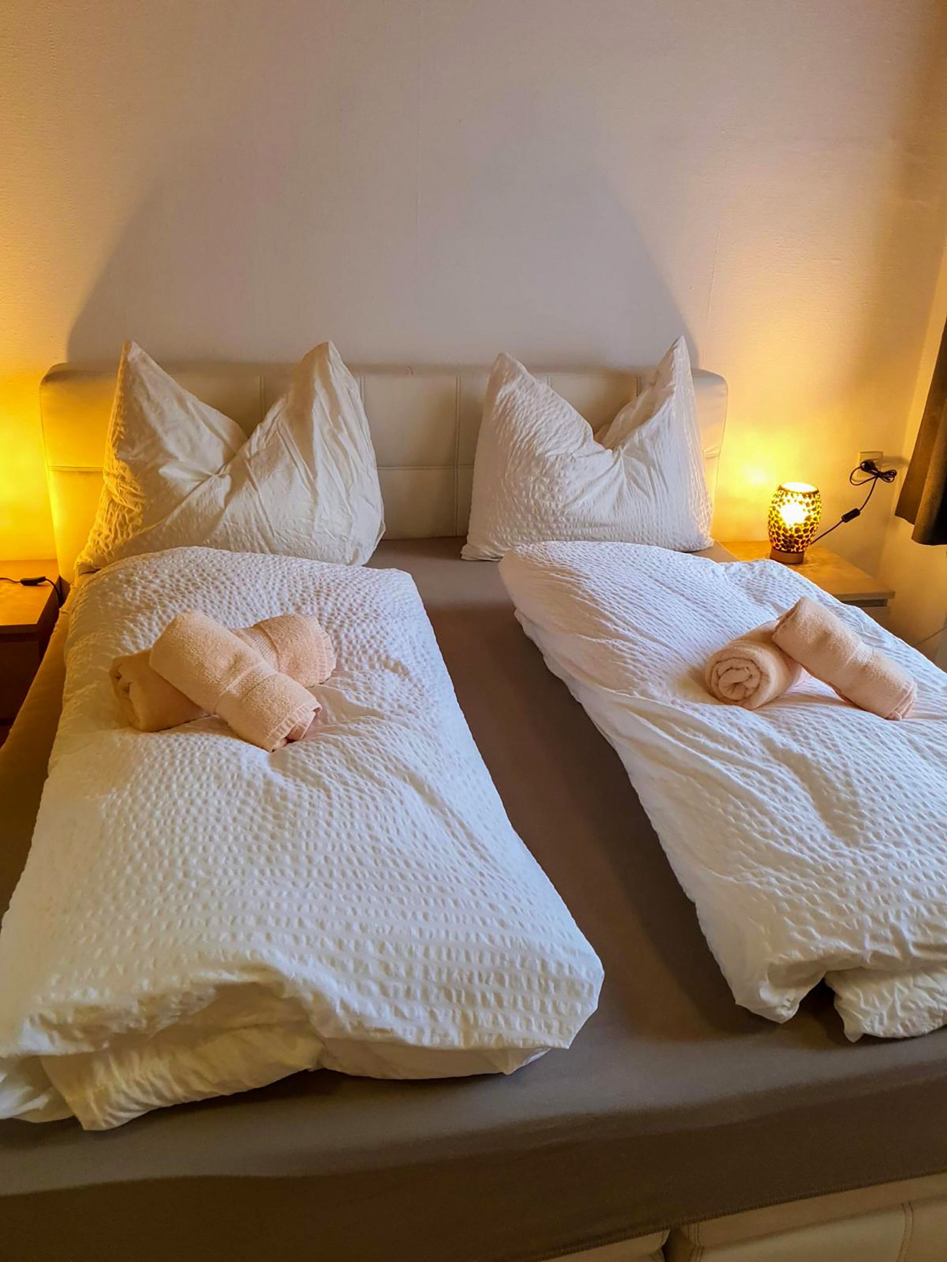 Ein Doppelbett mit weißer Bettwäsche und Kissen, eine Nachttischlampe sowie eine Steckdose an der Wand.