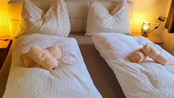 Ein Doppelbett mit weißer Bettwäsche und Kissen, eine Nachttischlampe sowie eine Steckdose an der Wand.