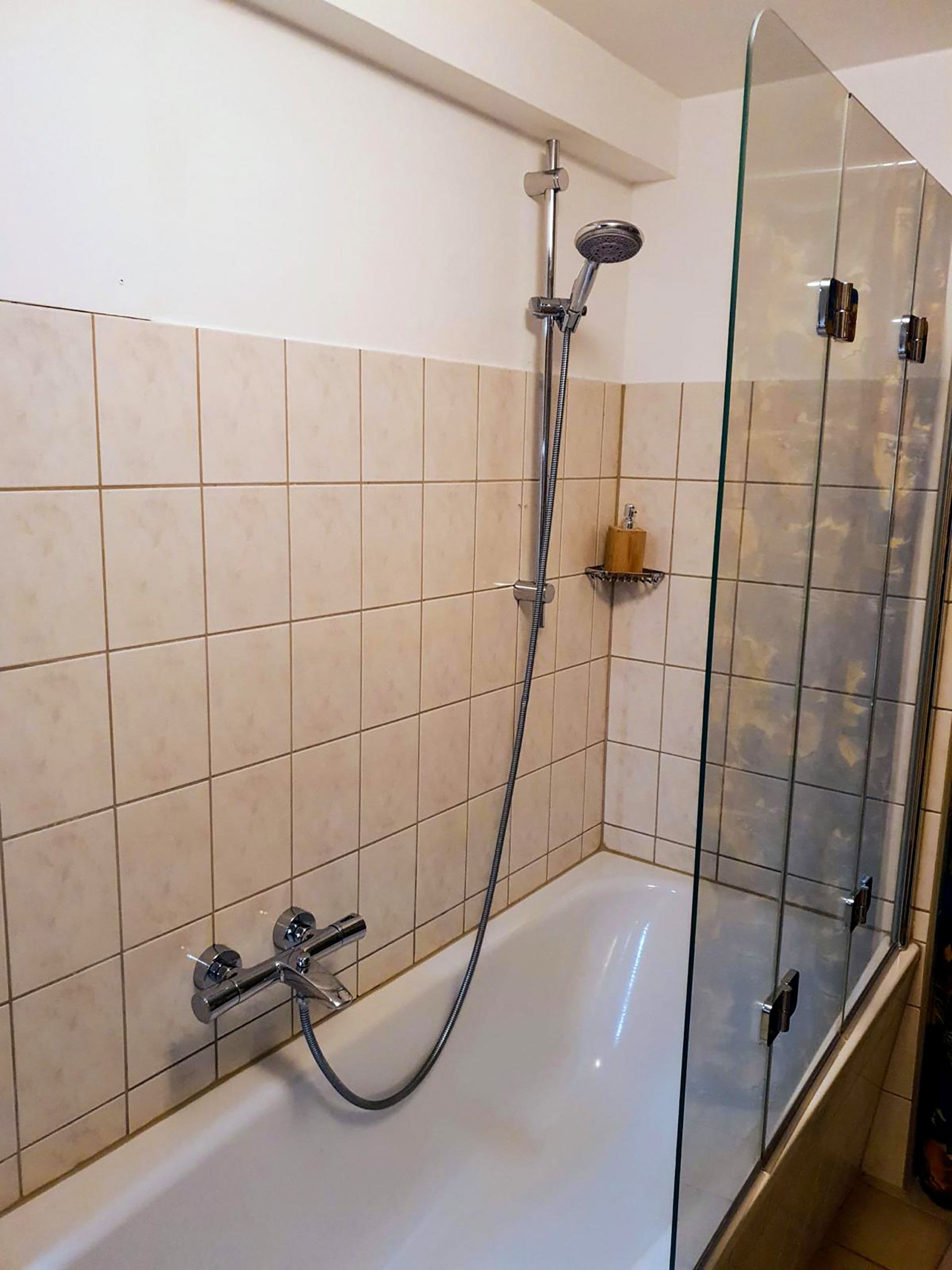 Ein Badezimmer mit einer gläsernen Duschkabine, einer weißen Badewanne und beige gefliesten Wänden.