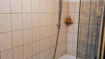 Ein Badezimmer mit einer gläsernen Duschkabine, einer weißen Badewanne und beige gefliesten Wänden.
