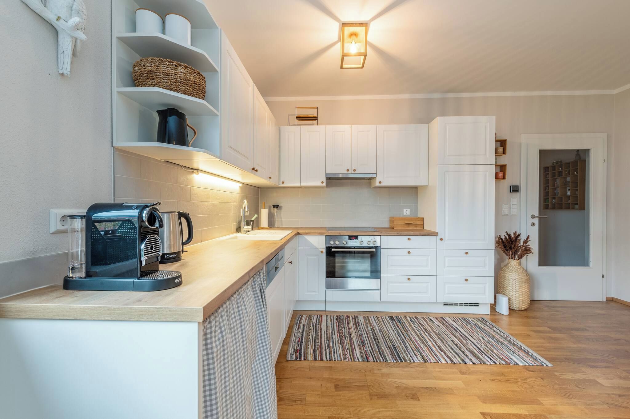 Een functionele keuken met witte kastjes, een inbouwoven, een koffieapparaat en een kleine koelkast.