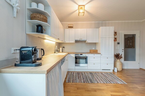 Een functionele keuken met witte kastjes, een inbouwoven, een koffieapparaat en een kleine koelkast.