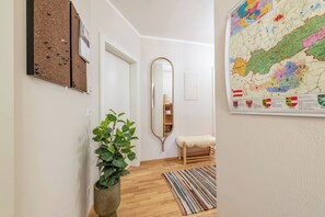Een gang met een houten vloer, een spiegel, een kamerplant, een gestreept tapijt en een kaart aan de muur.
