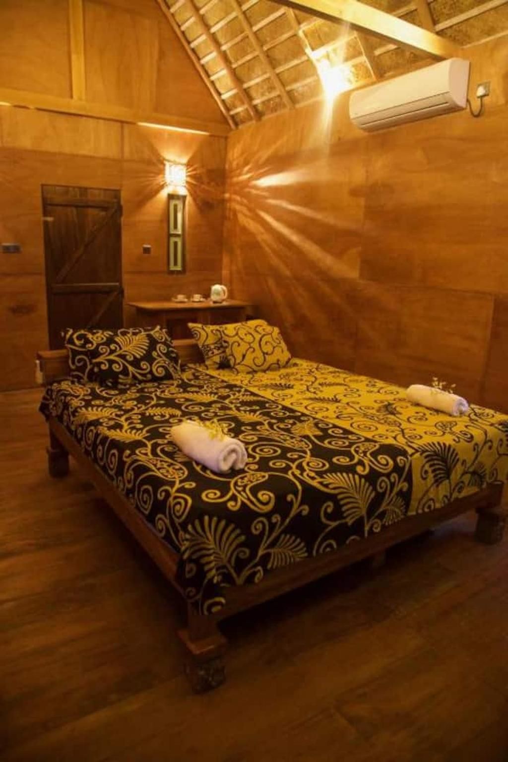 Habitación de madera con cama, mesita de noche, lámpara de pared y equipo de aire acondicionado.