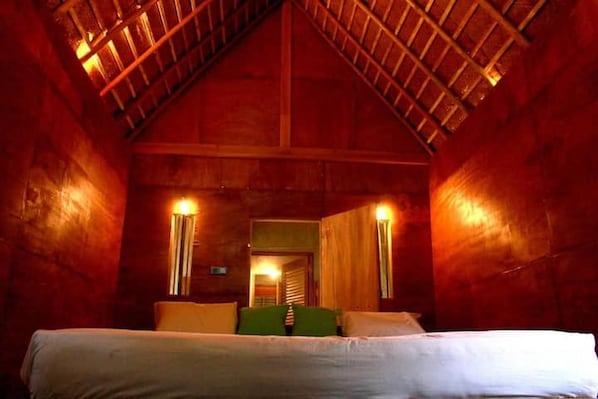 A room with a sloped ceiling, a bed with pillows, and two wall-mounted lamps. - Riverside AC cottage step to Sinharaja Forrest (SP)