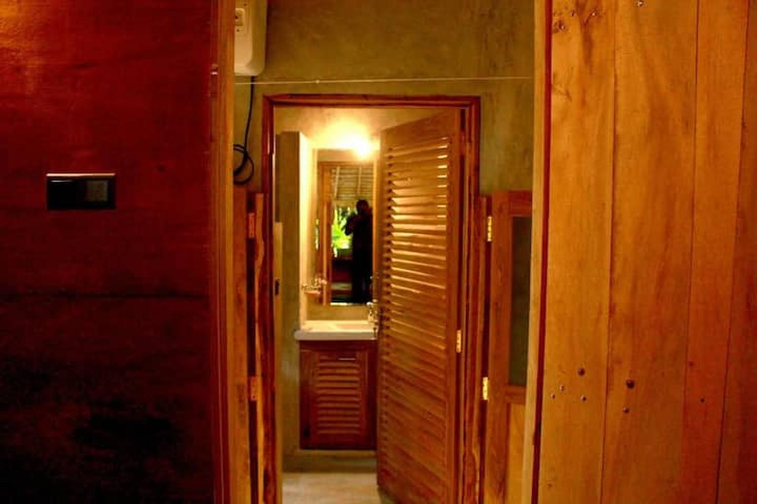 Un pasillo estrecho con puertas de madera y un baño visible con lavamanos y espejo.