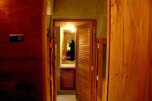 Passadís estret amb portes de fusta i un bany visible amb un lavabo i un mirall.