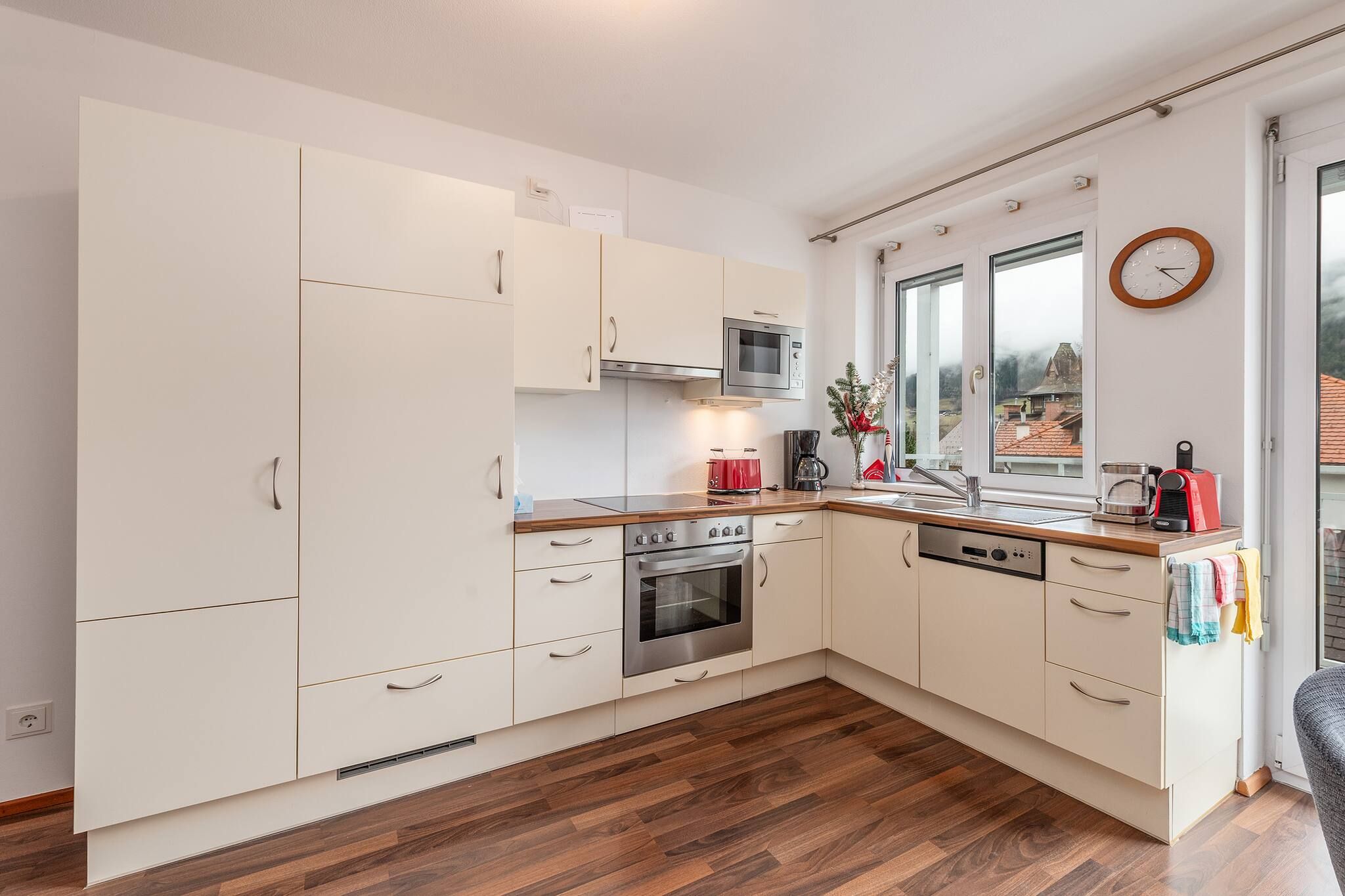Une cuisine moderne avec des meubles blancs, un four en acier inoxydable, un four à micro-ondes et une fenêtre donnant sur une maison.