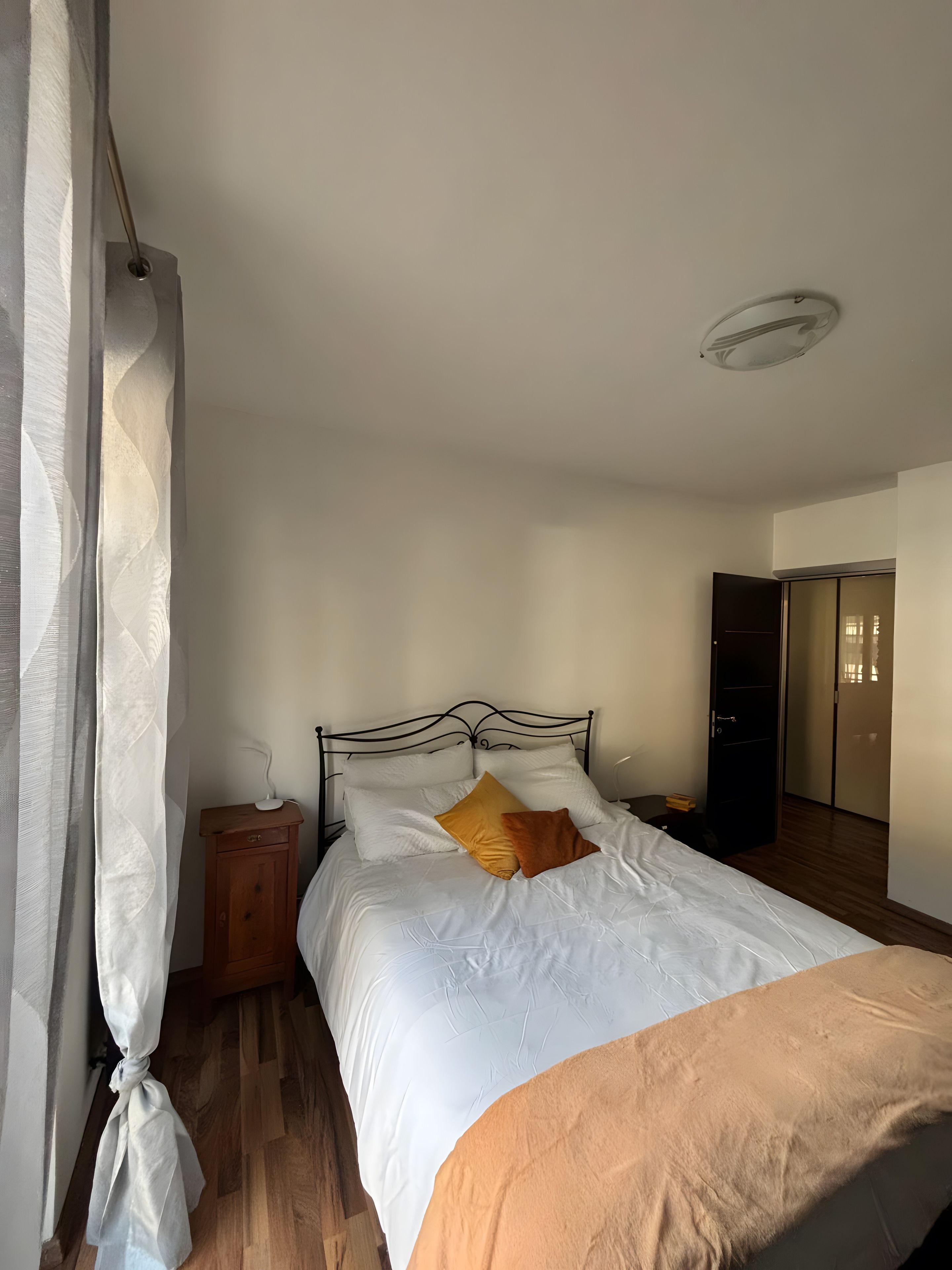 Una camera da letto con un letto, un comodino, un pavimento in legno e una porta che dà su un'altra stanza.
