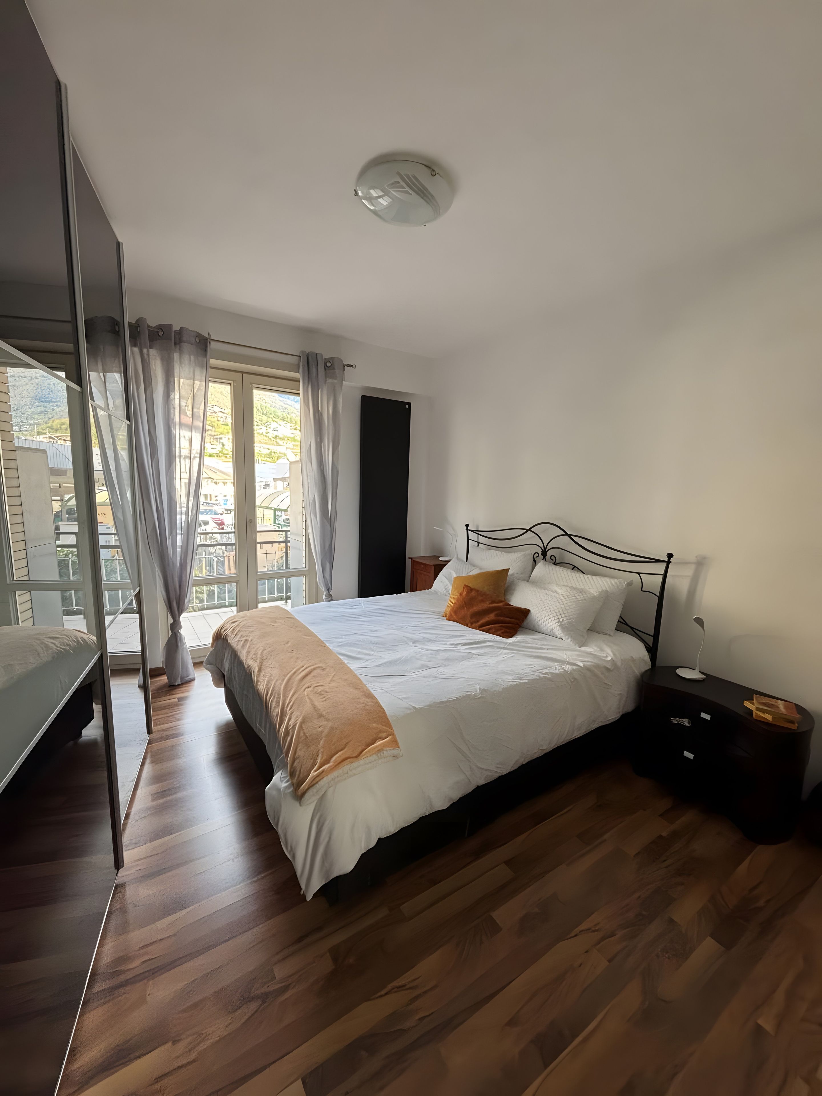 A bedroom with a bed, bedside table, and a view of the outdoors.