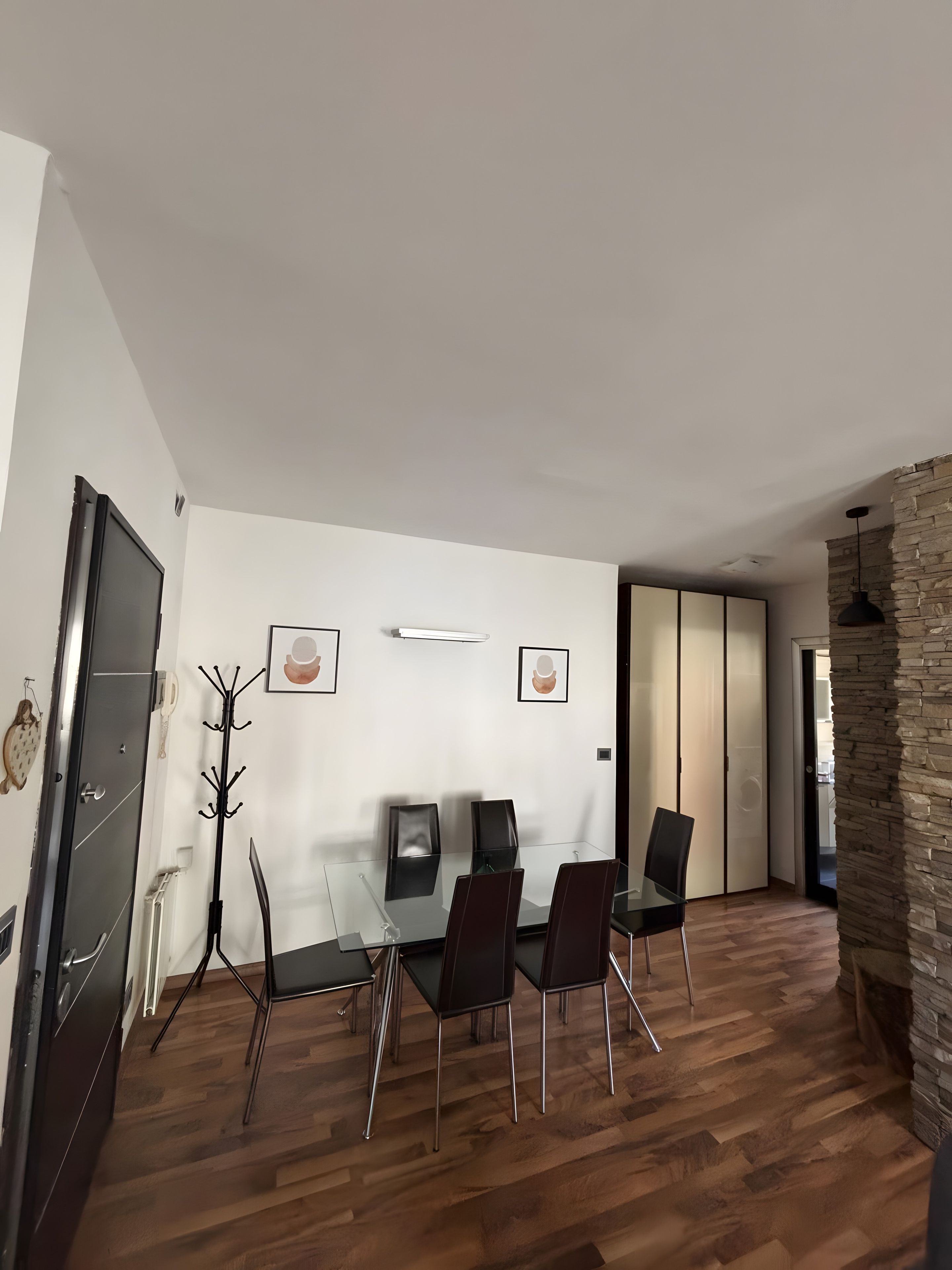 A modern dining area with a glass table and four chairs, a coat rack, and a stone accent wall.