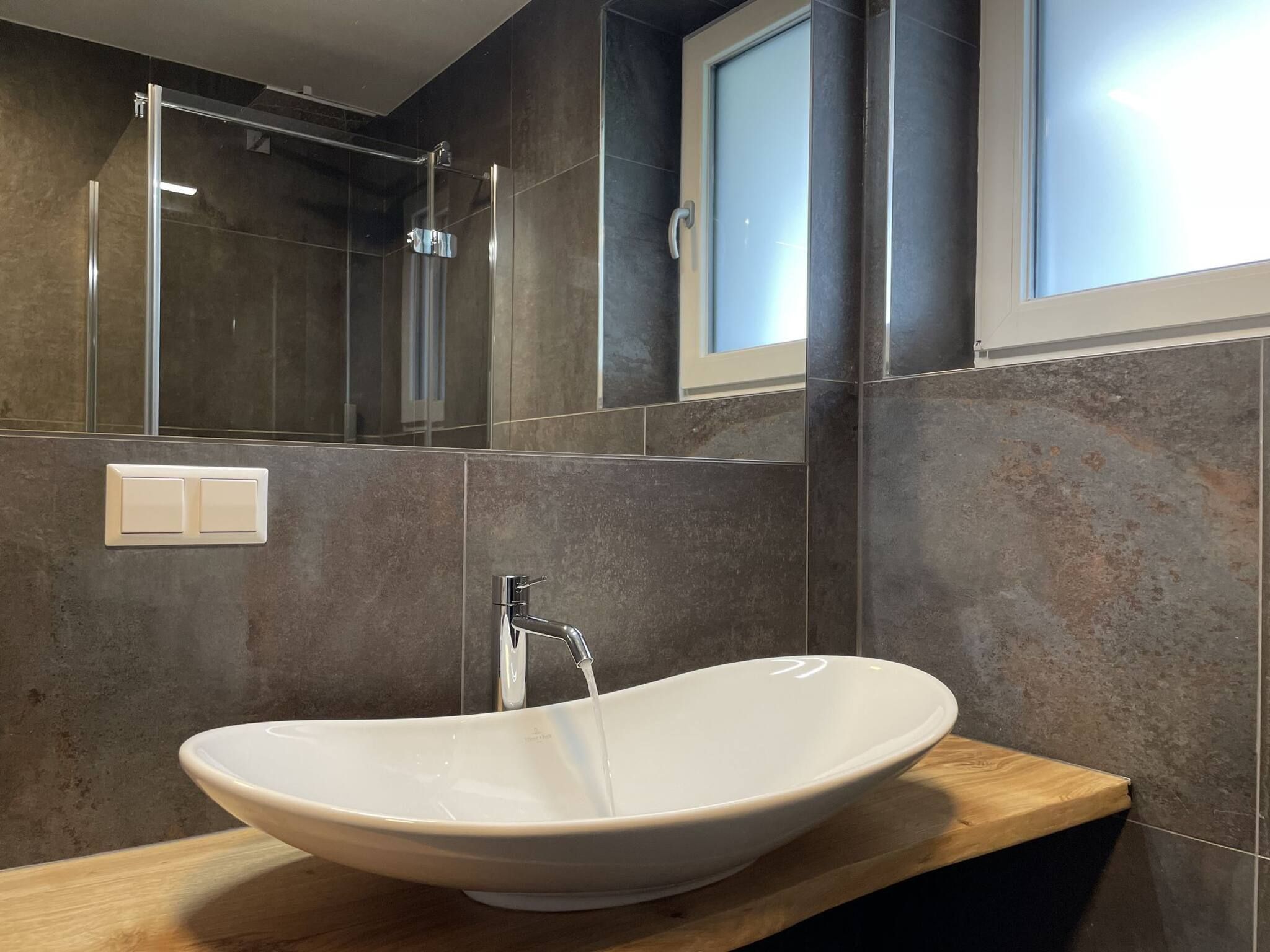 Ein modernes Badezimmer mit einem freistehenden Waschtisch, einer Handbrause und einem großen Spiegel.