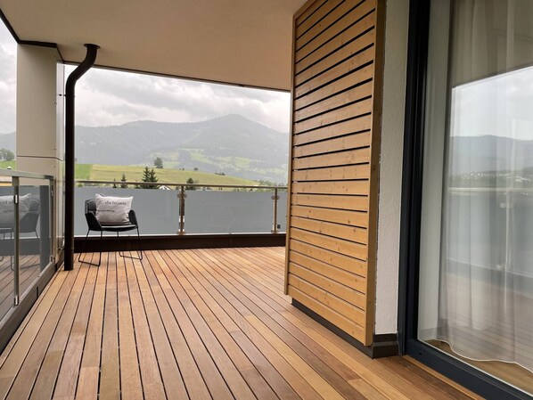 A balcony with a wooden floor, a chair, and a view of a lake and mountains. - Local View Apartment (Gröbming)
