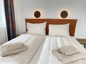 A double bed with white linens and two pillows, a brown headboard, and two bedside lamps. - Local View Apartment (Gröbming)