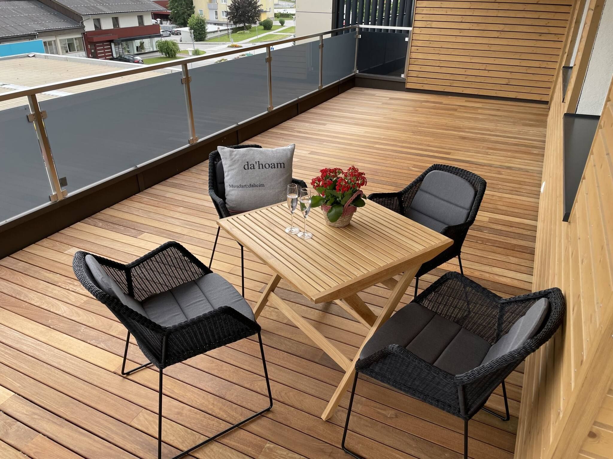 Eine Holzterrasse mit Tisch und Stühlen, einer Blumenvase und einem Kissen mit Schrift.