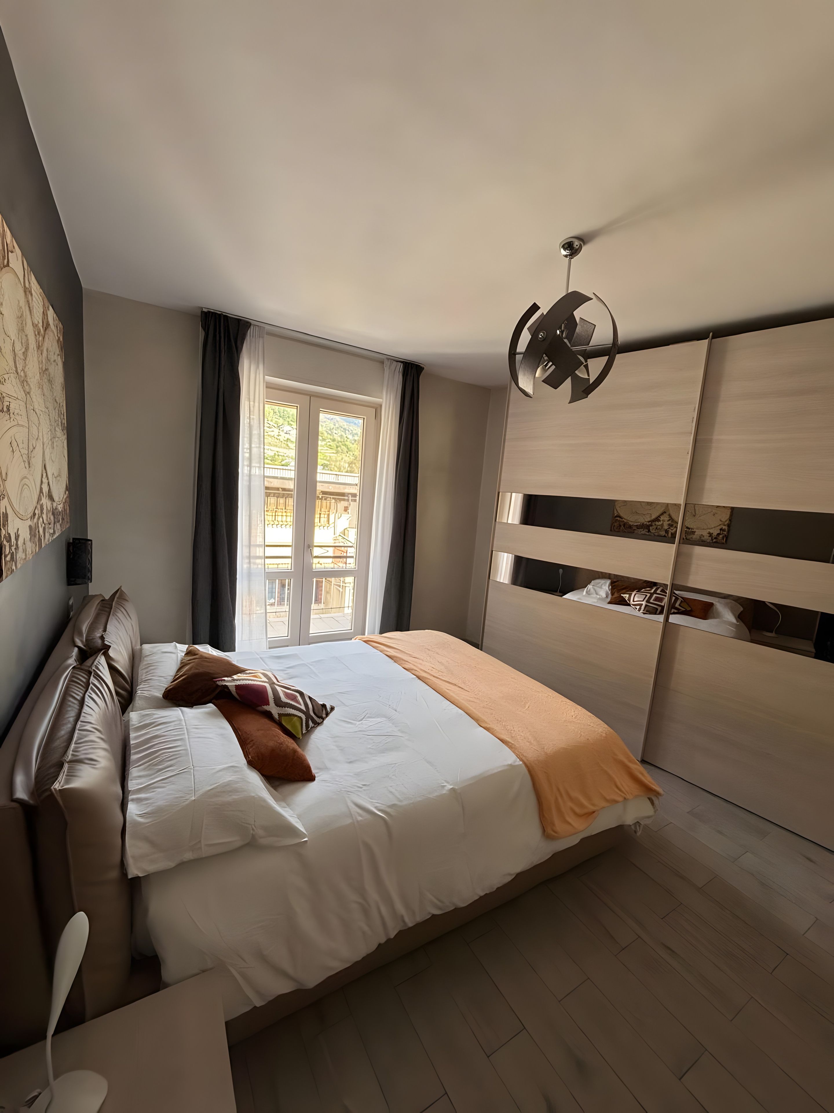 A bedroom with a bed, a bedside table, a wardrobe, a window, and a ceiling fan.
