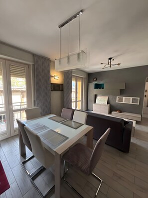 Una cocina moderna con zona de comedor, que incluye una mesa blanca, sillas grises y un sofá gris.