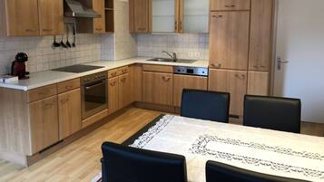 Une cuisine moderne avec des meubles en bois, un four encastré, un évier et un coin repas comprenant une table et des chaises.
