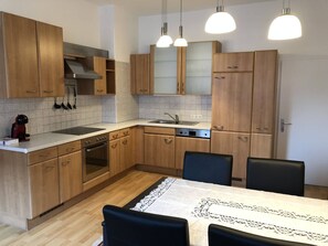 A modern kitchen with wooden cabinets, a built-in oven, a sink, and a dining area with a table and chairs. - Apartment zur Schmiede (Gröbming)