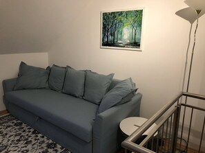 A grey sofa with multiple cushions, a small round table, a painting of a forest, and a modern floor lamp. - Apartment zur Schmiede (Gröbming)