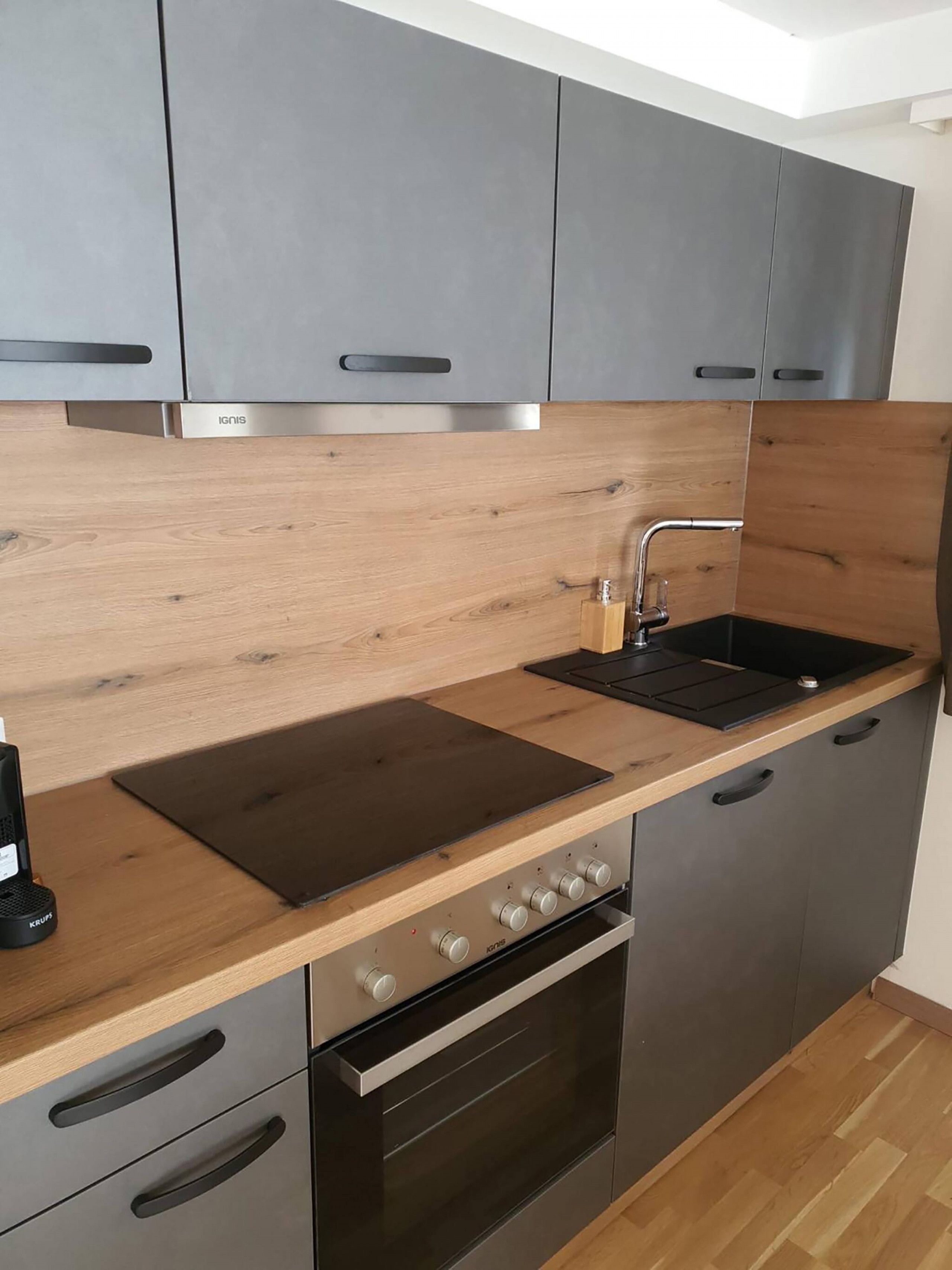 Eine moderne Küche mit grauen Schränken, einer Holzarbeitsplatte, einem eingebauten Backofen und einer Edelstahl-Dunstabzugshaube.