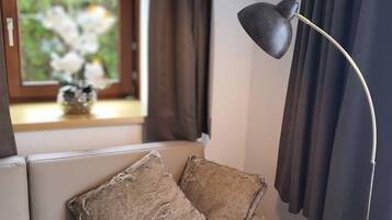 Ein modernes Wohnzimmer mit einer Couch, zwei Kissen, einer Stehlampe, einem Fenster mit Vorhängen und einer Vase mit Blumen.