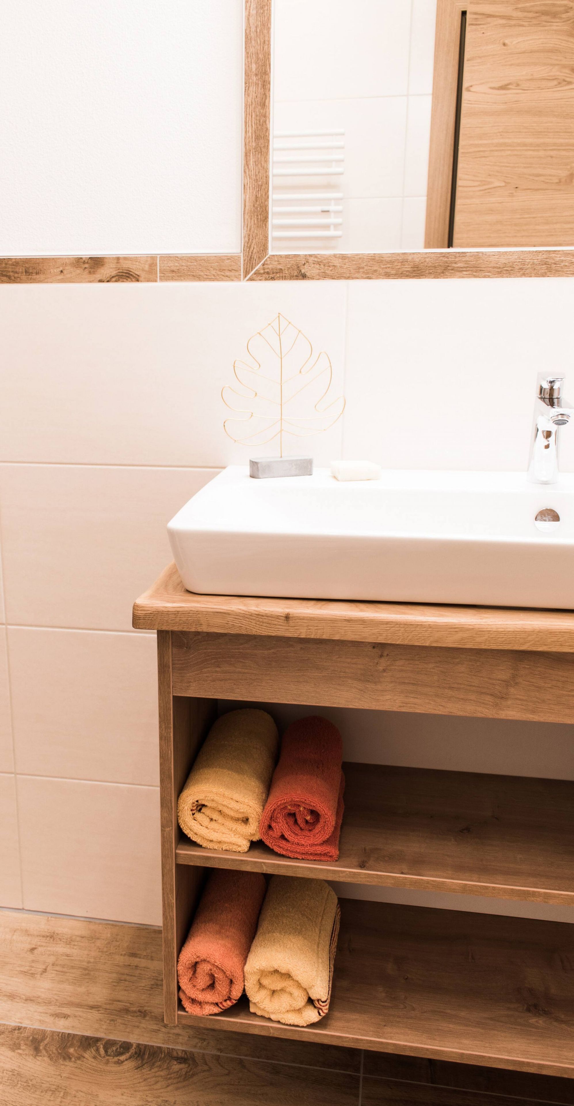 Une salle de bain avec un lavabo blanc, une étagère en bois et des serviettes.
