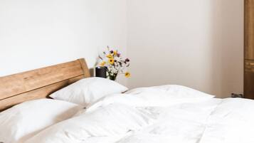 Une chambre à coucher avec une tête de lit en bois, un lit recouvert de linge de lit blanc, un luminaire suspendu et un vase rempli de fleurs placé sur une table de chevet.