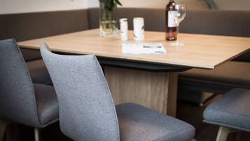 Un coin repas avec une table en bois, des chaises à revêtement gris, un vase contenant une fleur jaune et une bouteille de vin.