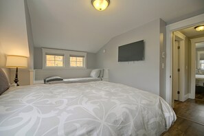 Un dormitorio con una cama grande, una mesita de noche, una lámpara, una ventana y un televisor de pantalla plana montado en la pared.