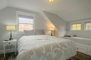 Ein Schlafzimmer mit einem großen Bett, zwei Nachttischen, einem Fenster und einer geneigten Decke.