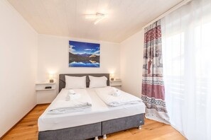 Habitación de hotel con cama, dos mesitas de noche con lámparas, un cuadro en la pared y cortina estampada.