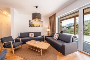 A modern living room with a sofa set, a coffee table, and a chair. There is a painting on the wall and a lamp on a side table. - Mountain Feelings Apartment (Gröbming)