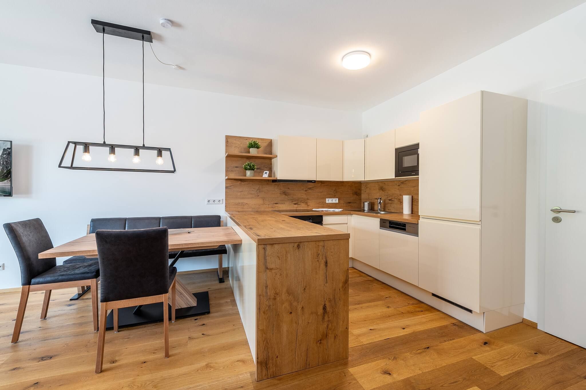 A modern kitchen with a wooden island, white cabinetry, and a dining area with a table and chairs.
