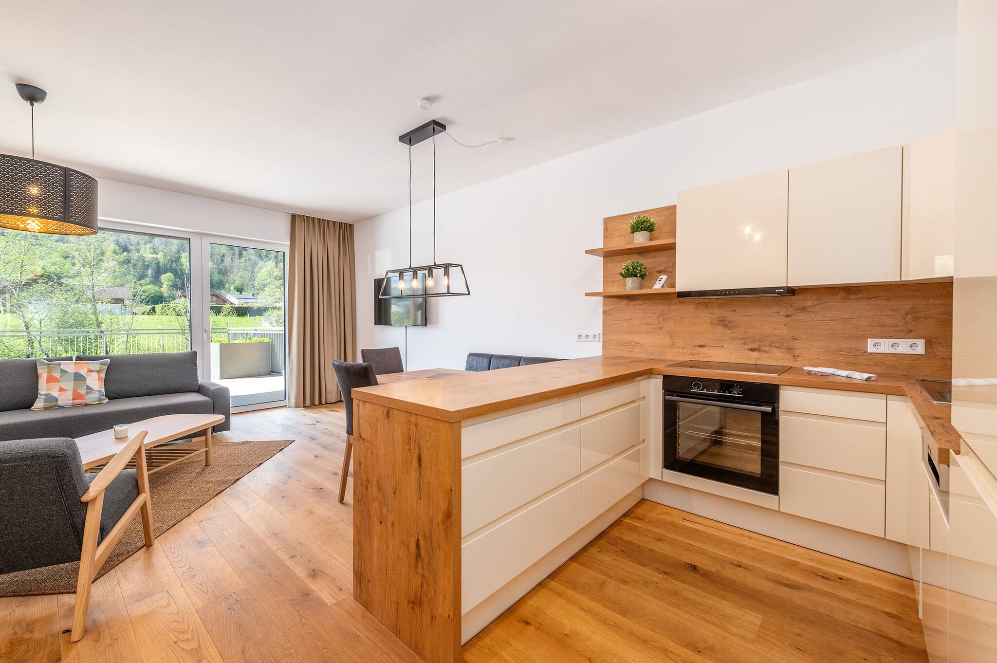 A modern kitchen with wooden cabinets, a built-in oven, and a dining area with a sofa and table.