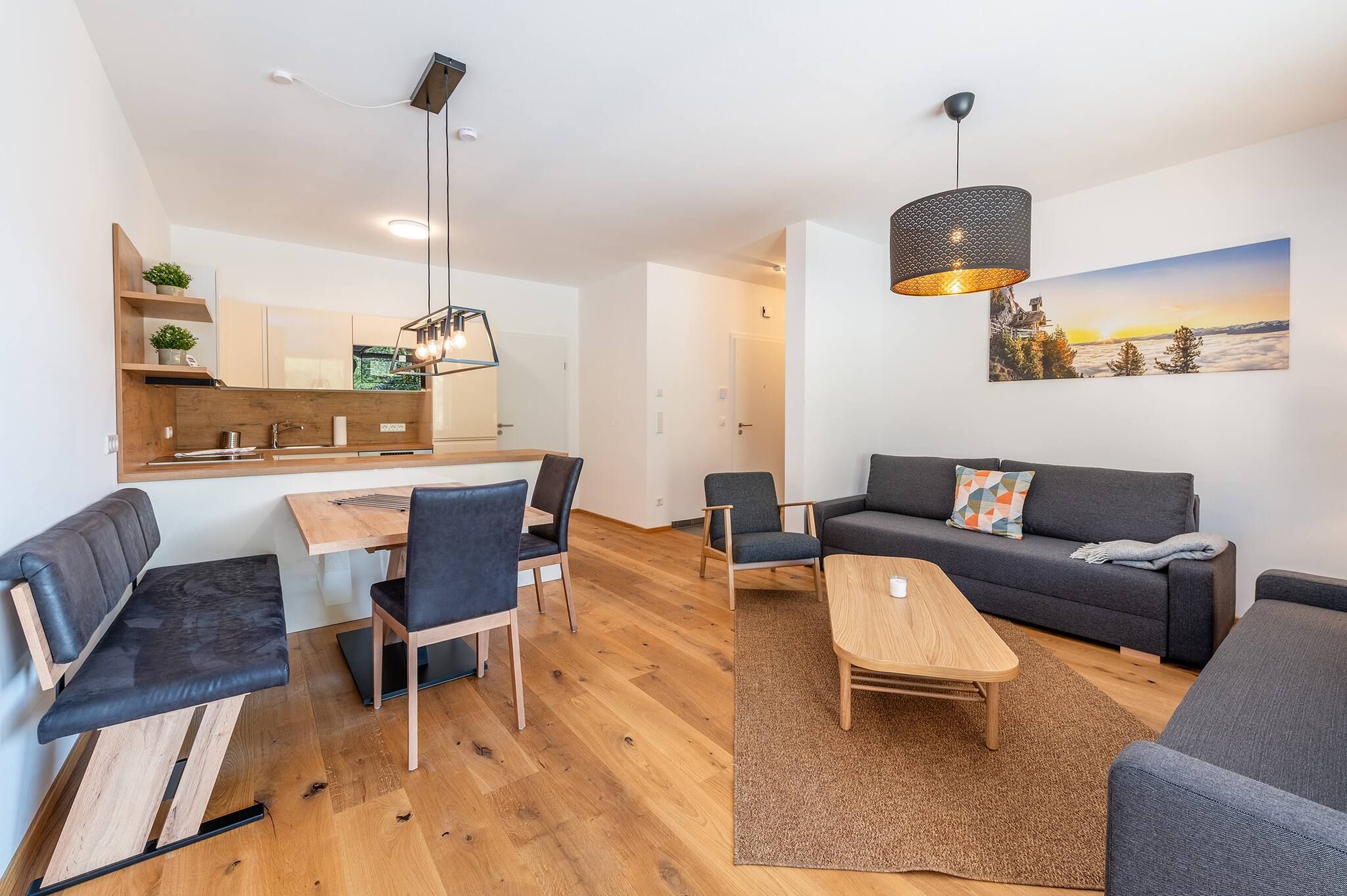 Ein moderner Wohnraum mit Essbereich, Sofa und einem Gemälde einer Berglandschaft.
