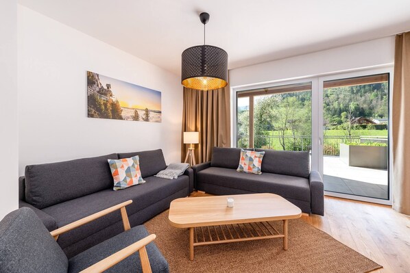 Ein modernes Wohnzimmer mit einem Ecksofa, einem Holztisch und einem großen Fenster mit Blick auf eine grüne Landschaft.