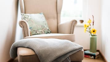 Un fauteuil confortable, agrémenté d’un plaid, d’un coussin et d’un vase de fleurs posé sur une petite table en bois.